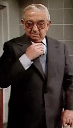 a man in a suit adjusts his tie while wearing glasses