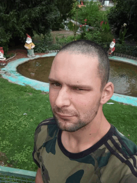 a man wearing a camouflage shirt is standing in front of a pond