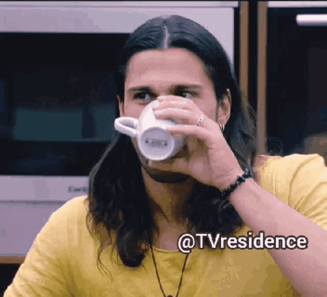 a man in a yellow shirt drinking from a white mug with the words @tvresidence on the bottom