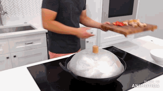 a man in a black shirt is holding a cutting board and a wok with a wooden lid on it