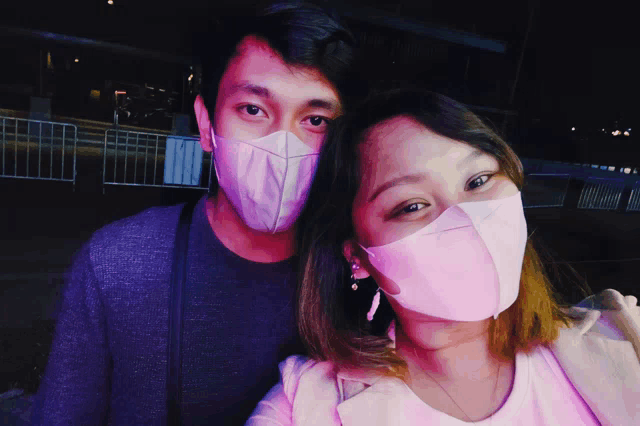 a man and a woman wearing pink face masks pose for a picture