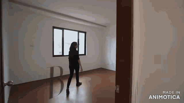 a woman is standing in an empty room looking out a window .
