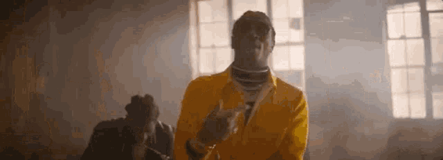 a man in a yellow jacket is smoking a cigarette in a dark room .