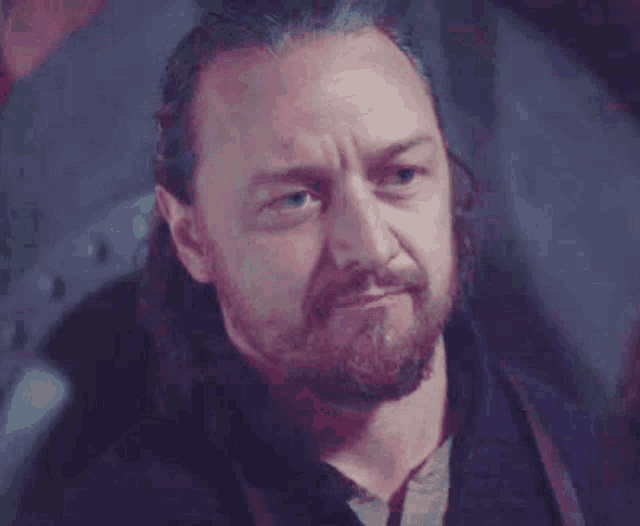 a man with a beard and long hair is looking at the camera and making a funny face .