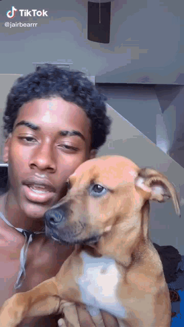a man without a shirt is holding a brown and white dog in his arms .
