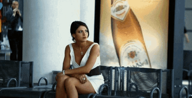 a woman in a white dress sits in front of a large advertisement for a beer