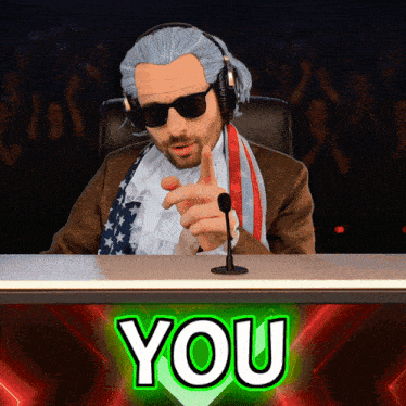 a man sitting at a desk with a green sign that says you on it