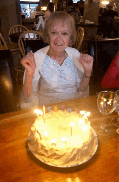 an elderly woman is sitting at a table with a birthday cake