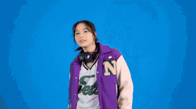 a woman wearing a purple varsity jacket and headphones .