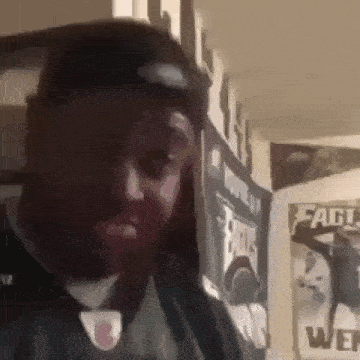 a man with a beard is standing in a room next to a wall with posters on it .