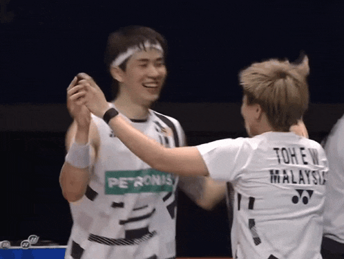 a man wearing a petronas shirt high fives another man wearing a tohew malaysia shirt