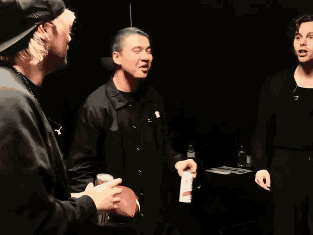 three men are standing in a dark room one is holding a football and the other is holding a can of pringles