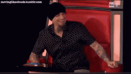 a man wearing a black hat and a black shirt is dancing in front of a red wall .