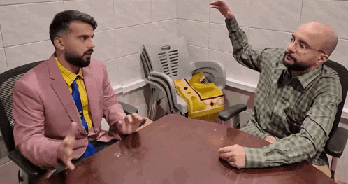 two men are sitting at a table with their arms in the air