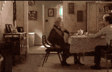 a man and an older woman sit at a table in a living room