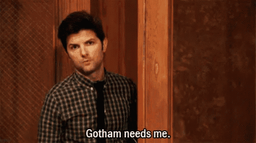 a man in a plaid shirt and tie is standing in front of a door and says gotham needs me .
