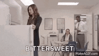 a woman is opening a refrigerator door in an office while a man stands behind her .