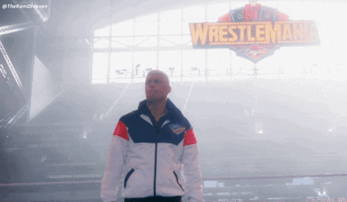a man in a jacket stands in front of a wrestlemania sign