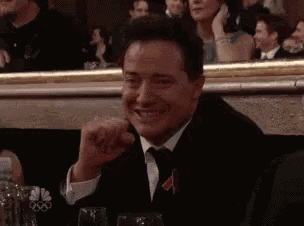 a man in a suit and tie is smiling while sitting at a table with glasses .