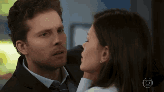 a man in a suit and tie kisses a woman in a white shirt on the neck