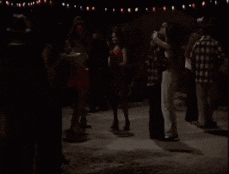 a man in a white tank top stands in front of a crowd of people dancing .