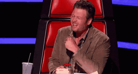 a man in a suit is sitting in a red chair and laughing while holding a cup of coffee .