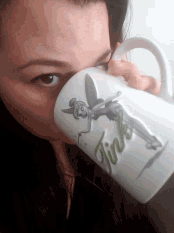 a woman is drinking from a mug that says tinkerbell on it
