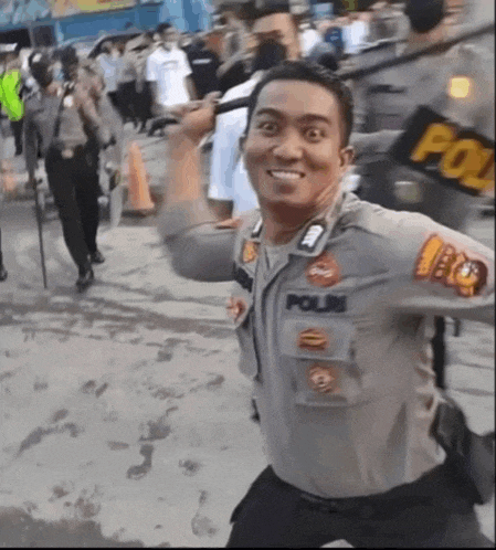 a police officer is smiling while holding a baton in front of a crowd of people .