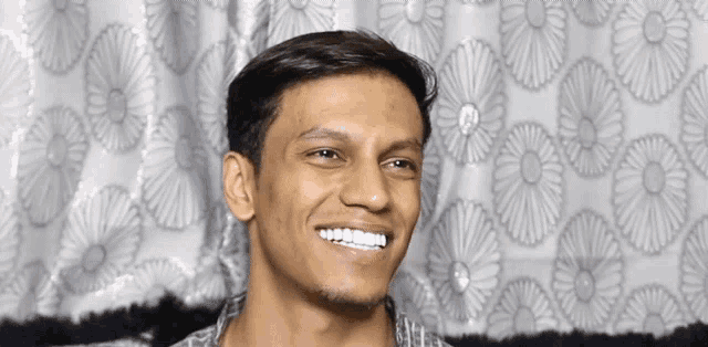 a young man is smiling in front of a floral patterned curtain