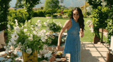 a woman in a blue dress is standing in front of a table with flowers on it