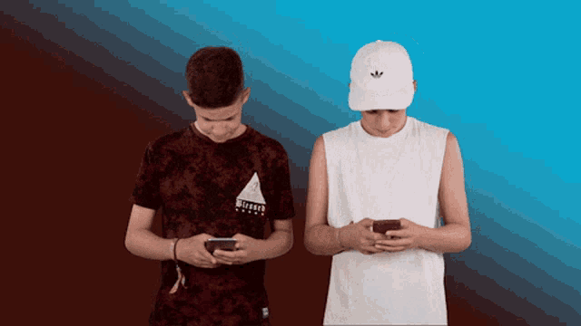 two boys looking at their cell phones one wearing a white adidas hat