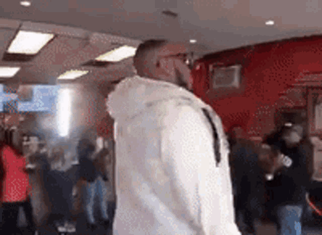 a man in a white hoodie is standing in a crowded room