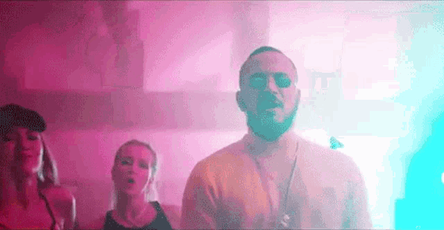 a man with a beard is standing next to two women in a pink and blue room .