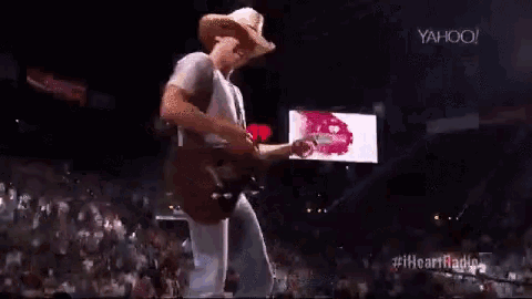 a man in a cowboy hat is playing a guitar on stage in front of a crowd .