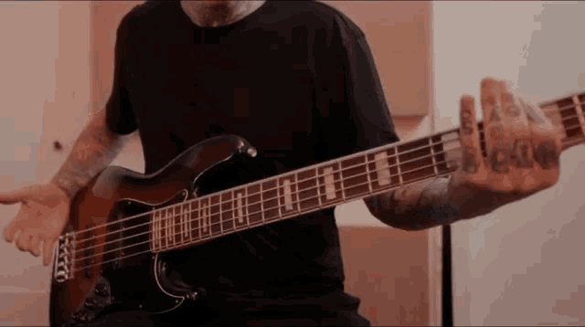 a man with tattoos on his arms is playing a bass guitar with the letter t on the strings