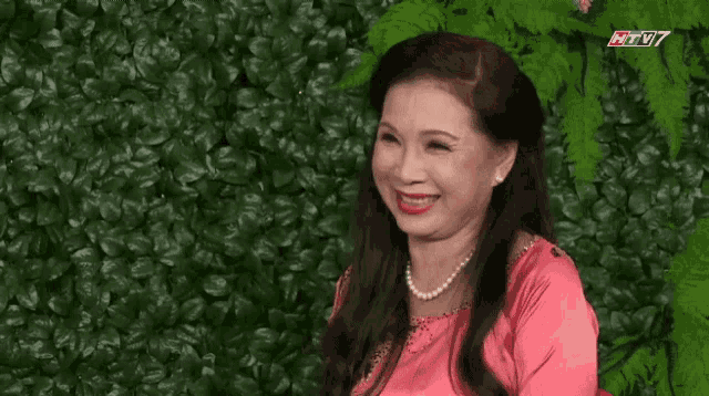 a woman laughs in front of a green wall with htv7 on the bottom