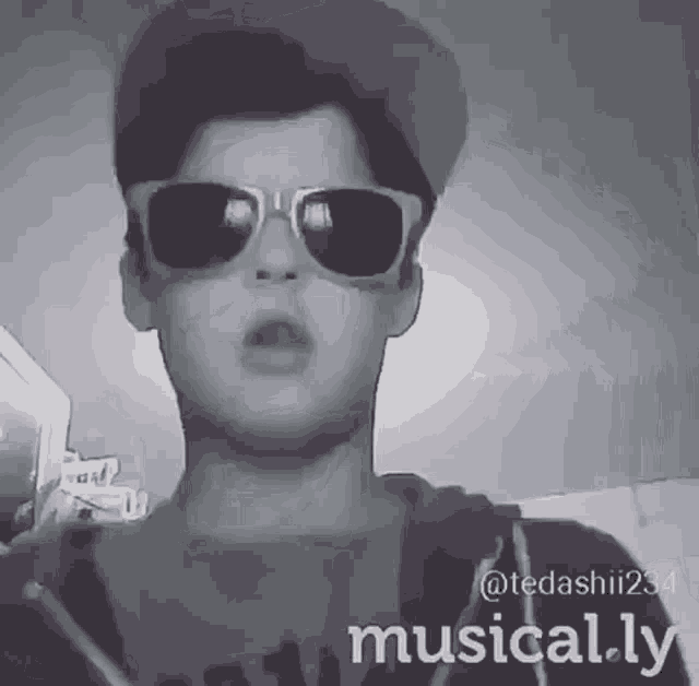 a black and white photo of a young man wearing sunglasses and a hat