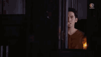 a man is brushing his teeth in a dark room while looking out of a window with a candle .