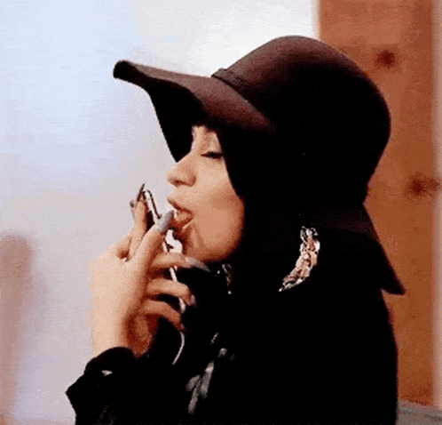 a woman wearing a hat is smoking a cigarette .