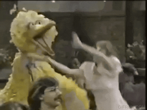 a group of people are dancing with a big bird mascot in a crowd .