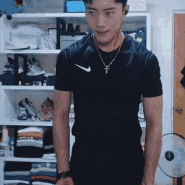 a man wearing a black nike shirt and a cross necklace is standing in front of a closet .