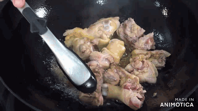 chicken is being cooked in a wok with tongs and the words made in animotica on the bottom