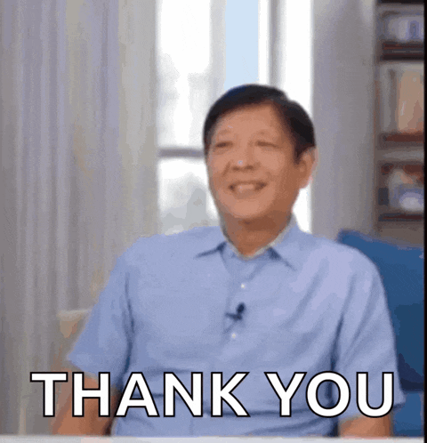 a man in a blue shirt is sitting at a table and smiling while saying thank you .