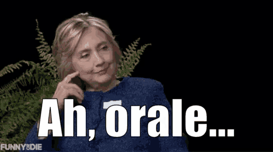 a woman in a blue sweater is sitting in front of a plant and says ah orale