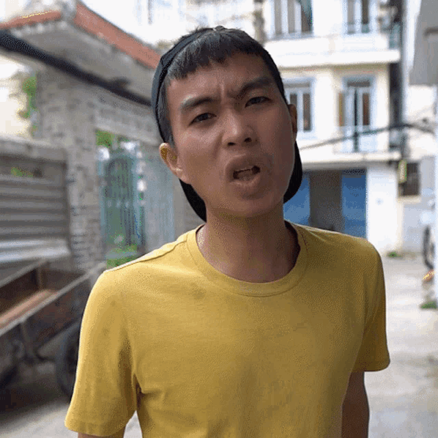 a young man wearing a yellow t-shirt and a black hat makes a funny face