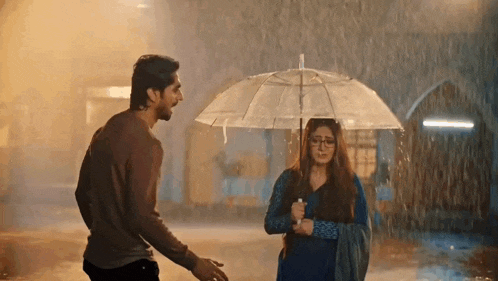 a man is holding an umbrella over a woman who is holding a clear umbrella in the rain .