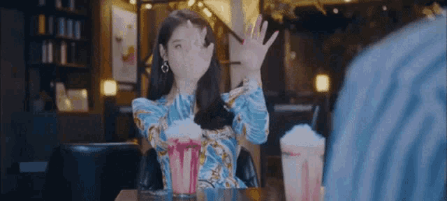 a woman in a blue dress is sitting at a table with popcorn and a cup of milkshake .