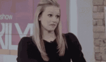 a woman is making a funny face while sitting in front of a pink sign .