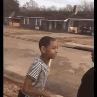a young boy in a striped shirt is walking down a street next to a house .