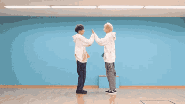 two men are giving each other a high five in a room with a blue wall